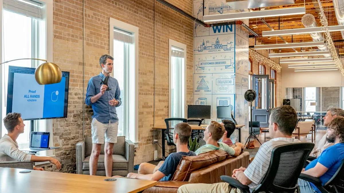 A small team in a brick-walled office listens to a man presenting at a screen