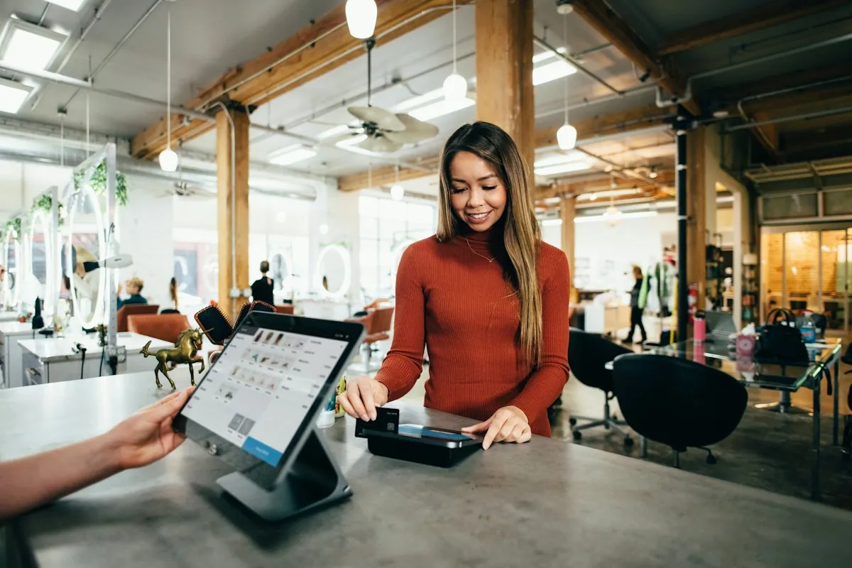 A woman pays by card at a checkout counter with a tablet register